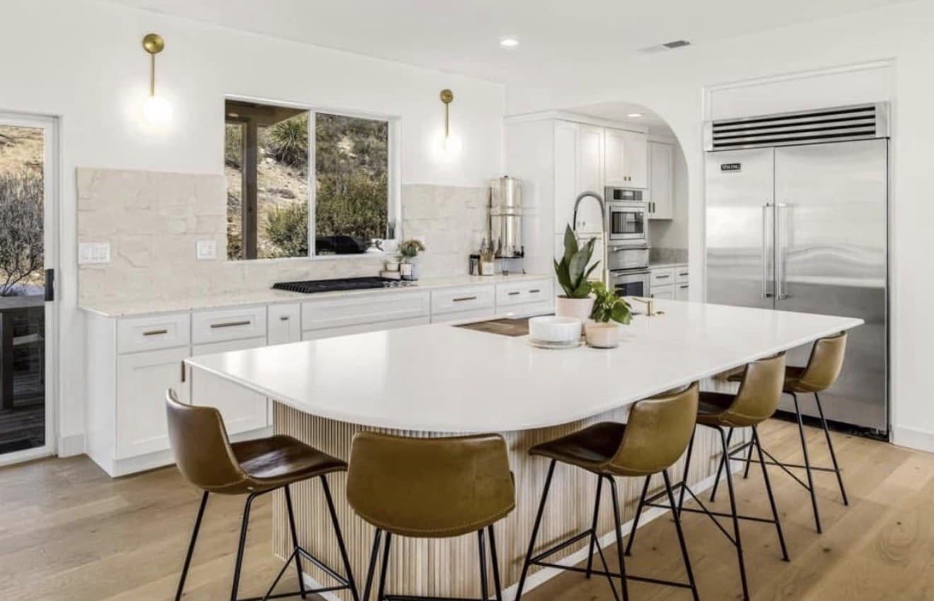 White kitchen with a fluted island and brown bar stools